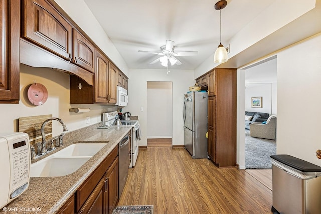 kitchen featuring appliances with stainless steel finishes, light stone counters, wood finished floors, pendant lighting, and a sink