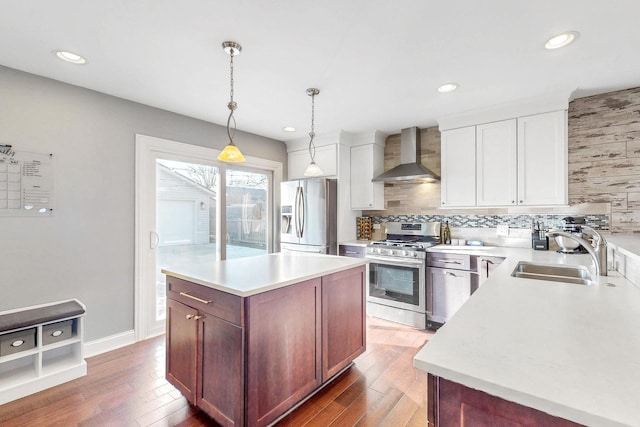 kitchen with wood finished floors, a sink, decorative backsplash, stainless steel appliances, and wall chimney exhaust hood