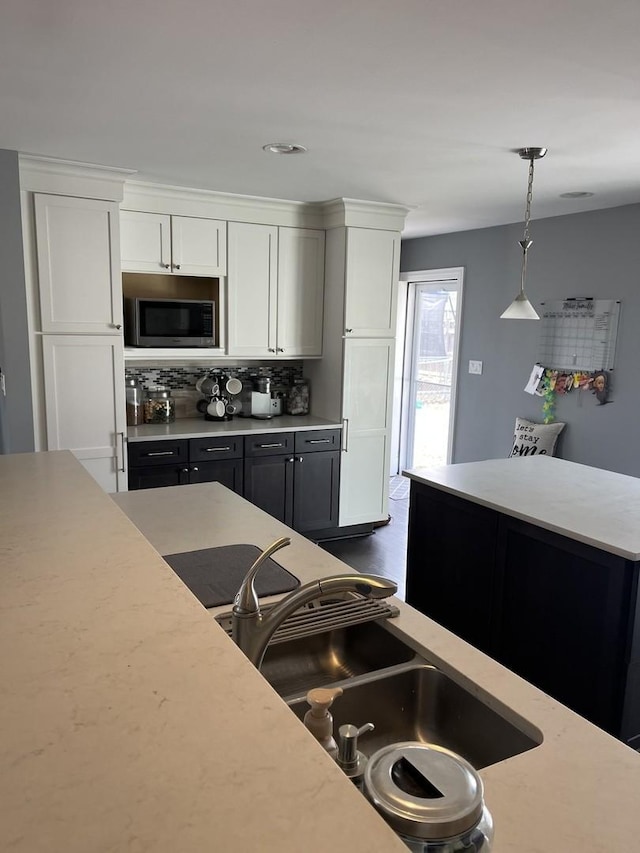 kitchen with stainless steel microwave, decorative light fixtures, light countertops, white cabinets, and a sink