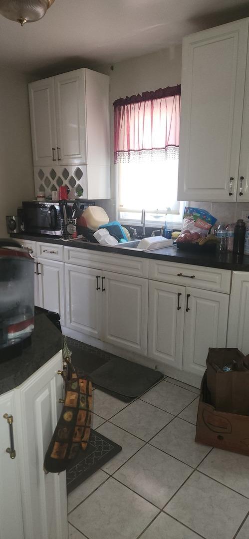 kitchen featuring dark countertops, light tile patterned floors, backsplash, and white cabinetry