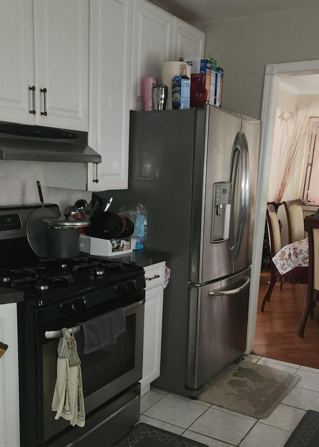 kitchen featuring under cabinet range hood, gas range oven, stainless steel fridge, light tile patterned flooring, and white cabinets