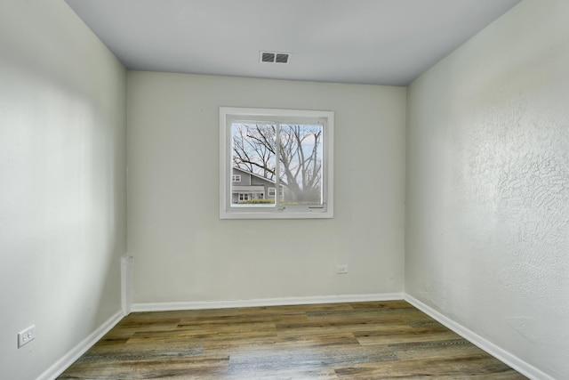 empty room featuring wood finished floors, visible vents, and baseboards