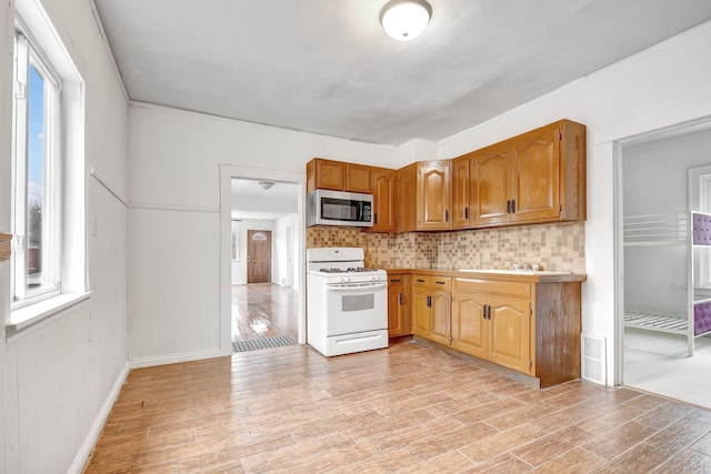 14719 Wood St, Harvey, IL 60426 - kitchen with white gas stove, light countertops, stainless steel microwave, backsplash, and light wood-style floors