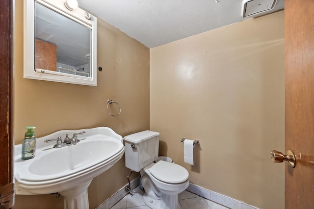 half bathroom featuring a sink, tile patterned flooring, toilet, and baseboards