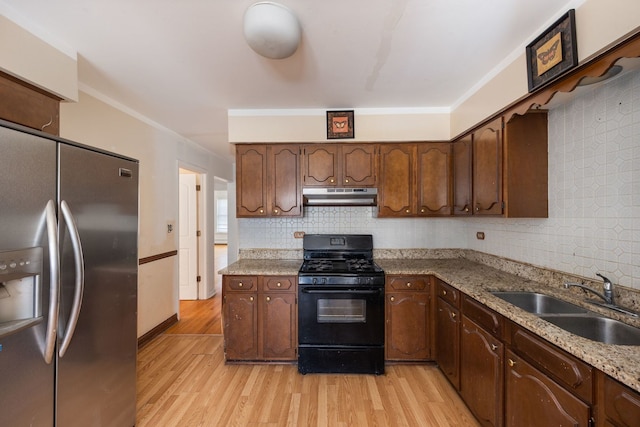 kitchen with light wood-style flooring, gas stove, a sink, stainless steel fridge, and under cabinet range hood