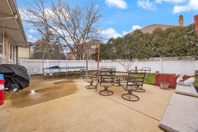 view of patio / terrace with a trampoline, outdoor dining area, a fenced backyard, and a grill