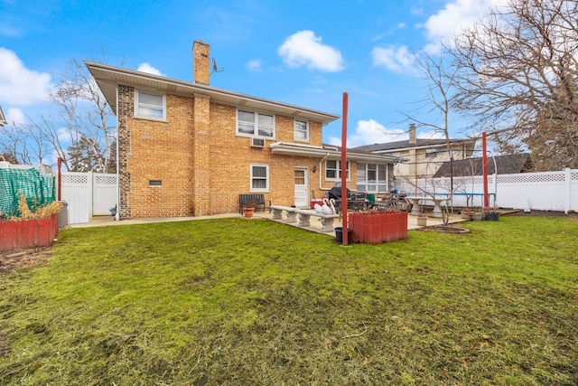 rear view of house featuring a patio, a fenced backyard, brick siding, a trampoline, and a chimney