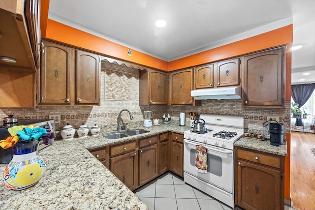 kitchen with light tile patterned floors, under cabinet range hood, a sink, tasteful backsplash, and white gas range