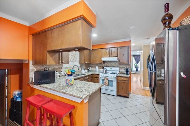 kitchen with white gas range, freestanding refrigerator, a sink, a peninsula, and under cabinet range hood