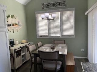 dining space featuring lofted ceiling, a notable chandelier, dark wood-style floors, and baseboards