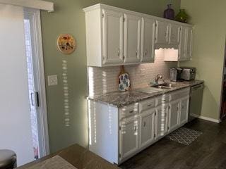 kitchen with dark wood-style flooring, white cabinetry, baseboards, backsplash, and dishwasher