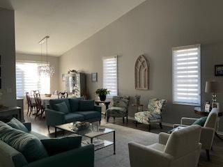 living room featuring high vaulted ceiling, plenty of natural light, a chandelier, and wood finished floors