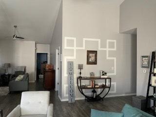 living room featuring ceiling fan, dark wood-type flooring, a high ceiling, and baseboards