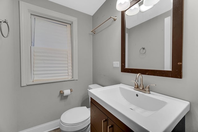 half bath with baseboards, vanity, and toilet