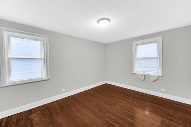 unfurnished room with dark wood-type flooring, visible vents, and baseboards