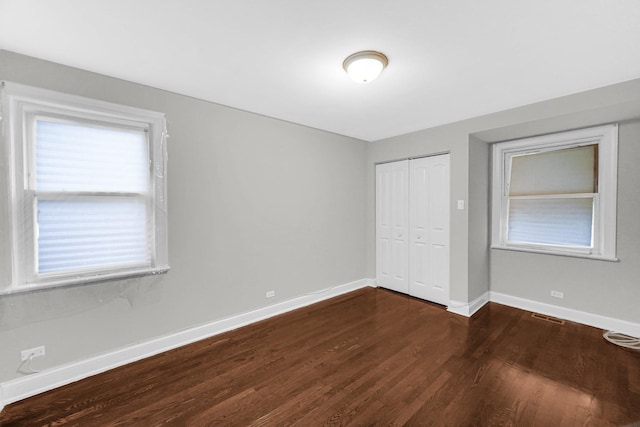 unfurnished bedroom with dark wood-style floors, baseboards, visible vents, and a closet