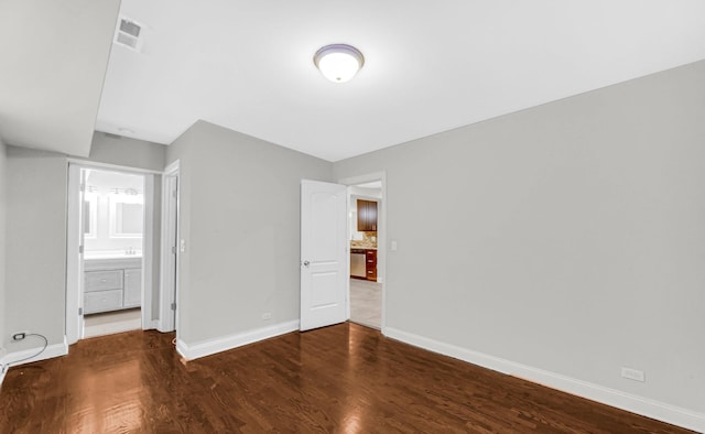 unfurnished bedroom featuring ensuite bath, wood finished floors, and baseboards