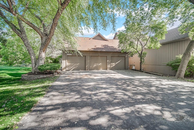 exterior space with aphalt driveway, a front yard, a shingled roof, and an attached garage