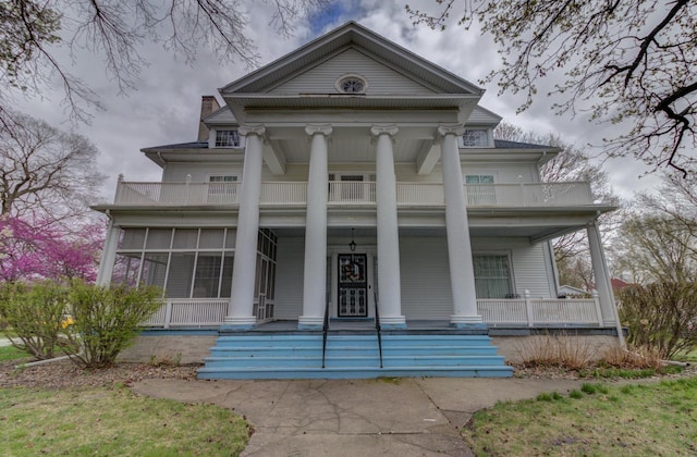 greek revival inspired property with a balcony, covered porch, and a chimney