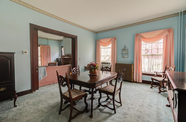 dining space featuring radiator, light carpet, crown molding, and baseboards