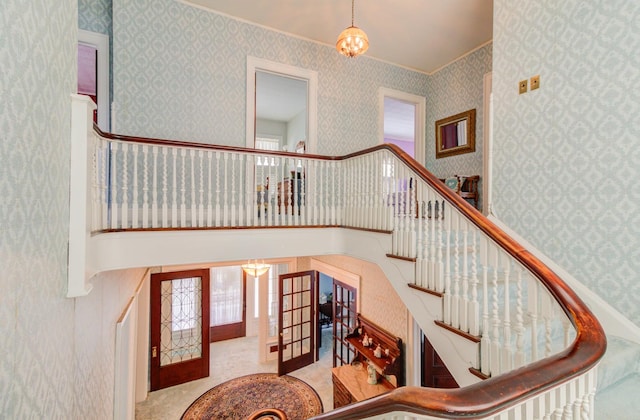 stairway with a notable chandelier, carpet floors, a high ceiling, french doors, and wallpapered walls