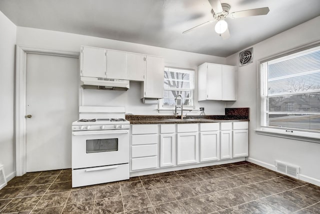 kitchen with white range with gas stovetop, dark countertops, under cabinet range hood, white cabinetry, and a sink