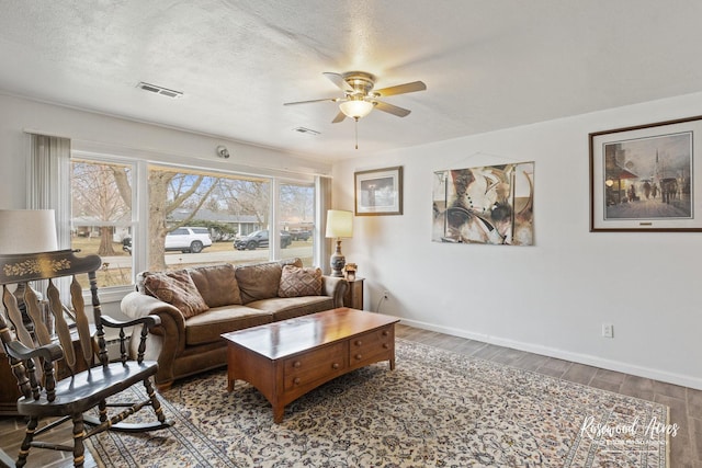 living room with baseboards, a textured ceiling, visible vents, and wood finished floors