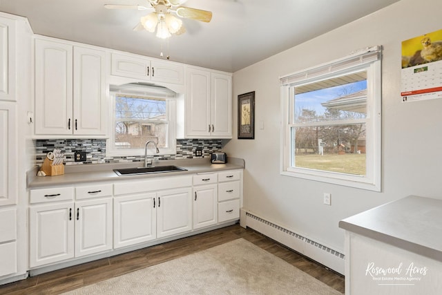 kitchen with tasteful backsplash, wood finished floors, light countertops, a baseboard heating unit, and a sink