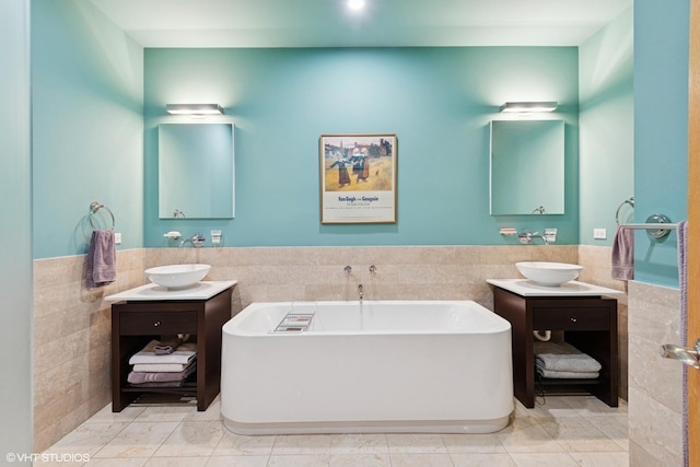 bathroom with a freestanding tub, a wainscoted wall, a sink, and tile walls