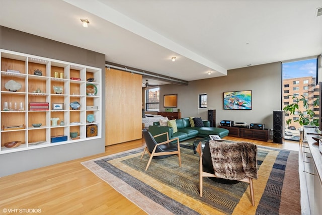 living area featuring beam ceiling, a barn door, plenty of natural light, and wood finished floors