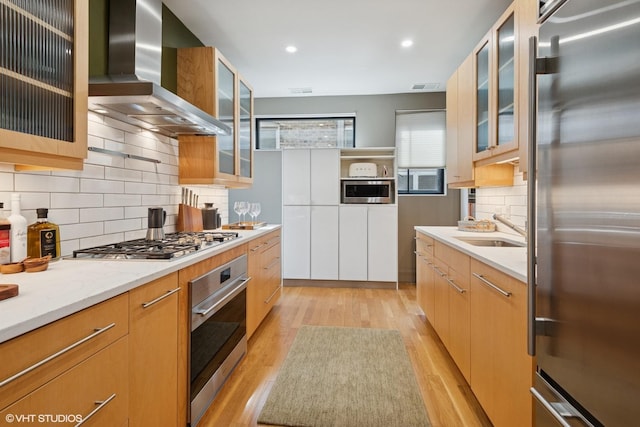 kitchen featuring visible vents, appliances with stainless steel finishes, a sink, light wood-type flooring, and wall chimney exhaust hood