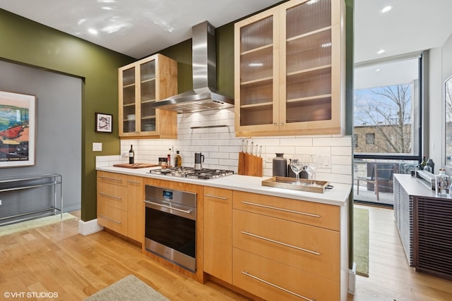 kitchen featuring stainless steel appliances, light wood-style floors, wall chimney exhaust hood, and decorative backsplash