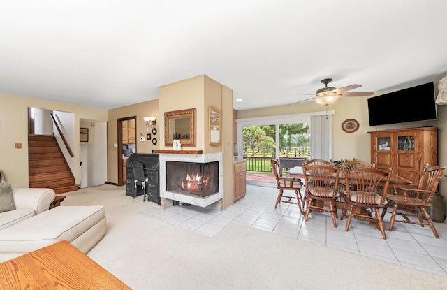 living room with light carpet, ceiling fan, stairway, a multi sided fireplace, and light tile patterned floors