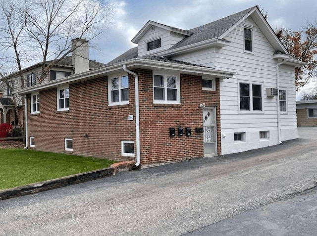 view of side of property with a yard, brick siding, a chimney, and a wall unit AC