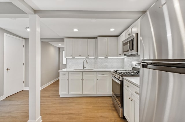 kitchen with stainless steel appliances, light countertops, light wood-style flooring, white cabinets, and a sink