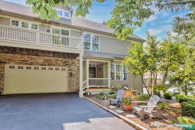 view of front of house with aphalt driveway, an attached garage, a balcony, stone siding, and roof with shingles