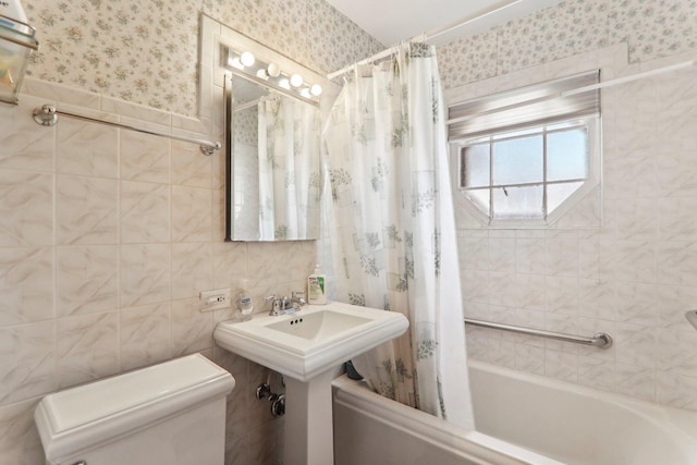 full bath featuring wallpapered walls, tile walls, toilet, shower / bathtub combination with curtain, and a sink