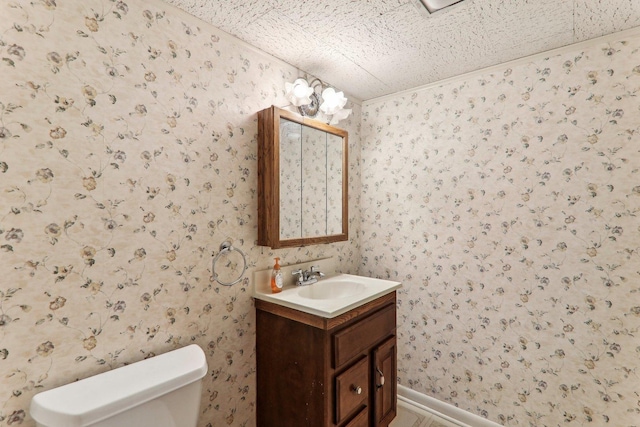 bathroom with vanity, toilet, and wallpapered walls