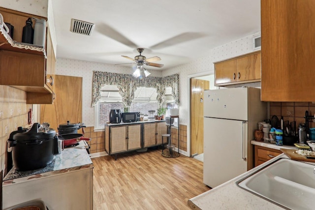 kitchen featuring visible vents, brown cabinetry, freestanding refrigerator, black microwave, and wallpapered walls