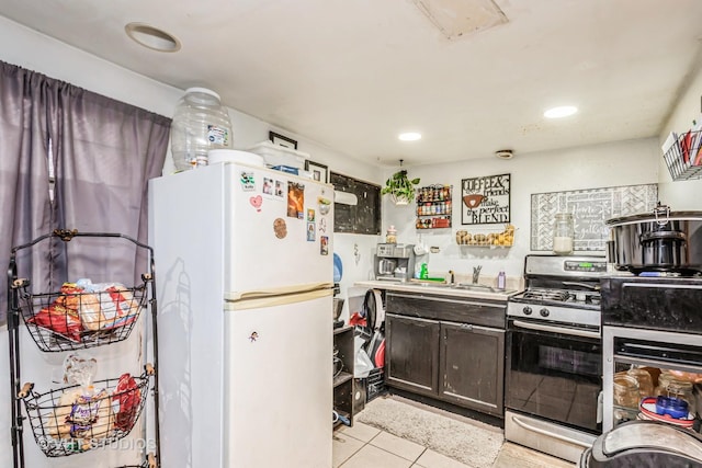 kitchen featuring stainless steel gas range oven, light tile patterned flooring, a sink, dark brown cabinets, and freestanding refrigerator