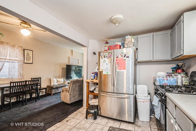 kitchen featuring black gas range, freestanding refrigerator, light countertops, gray cabinetry, and light tile patterned flooring