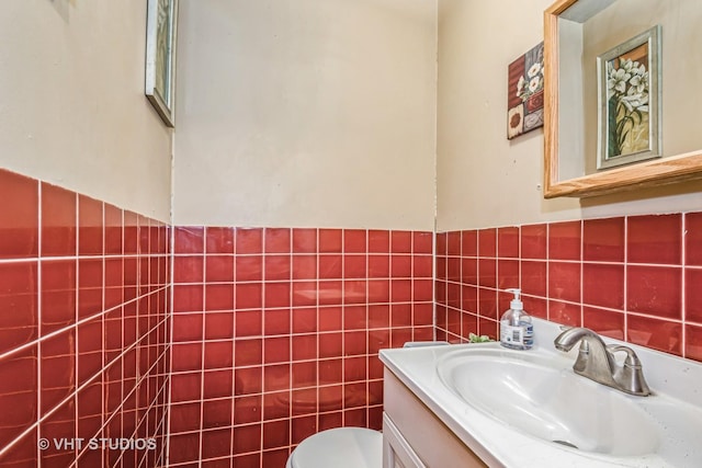 half bath with toilet, wainscoting, vanity, and tile walls