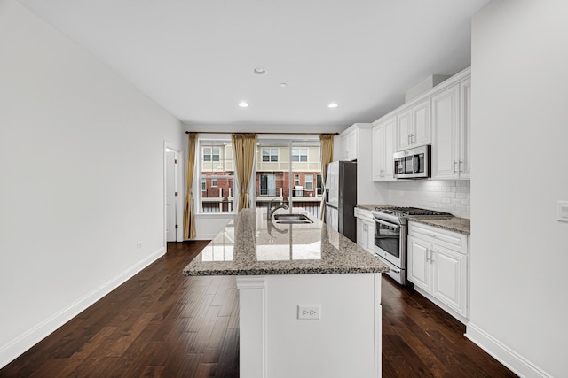 kitchen featuring appliances with stainless steel finishes, an island with sink, backsplash, and dark wood finished floors