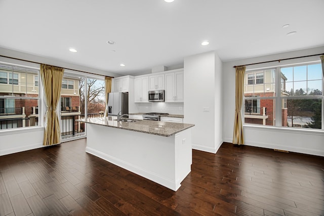 kitchen with stainless steel appliances, dark wood-style flooring, a sink, and a center island with sink