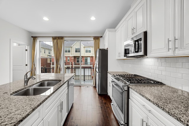 kitchen featuring dark wood finished floors, backsplash, appliances with stainless steel finishes, white cabinetry, and a sink