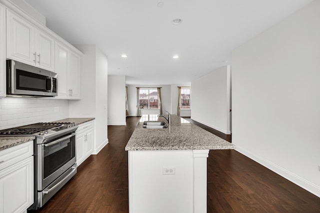 kitchen with dark wood-style flooring, a sink, appliances with stainless steel finishes, backsplash, and light stone countertops