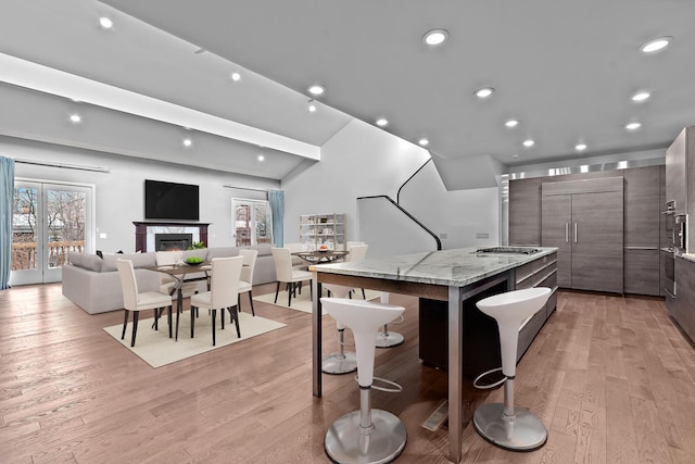 kitchen featuring paneled refrigerator, light wood-type flooring, modern cabinets, a glass covered fireplace, and a center island