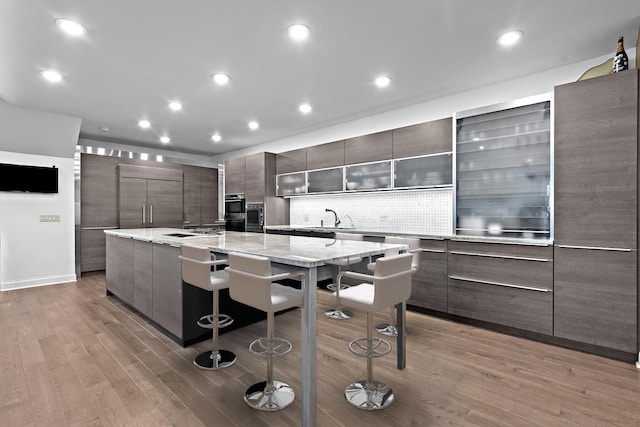 kitchen featuring a breakfast bar area, a sink, built in fridge, modern cabinets, and light wood-type flooring