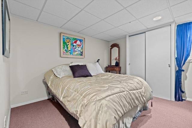 carpeted bedroom featuring a paneled ceiling, baseboards, and a closet