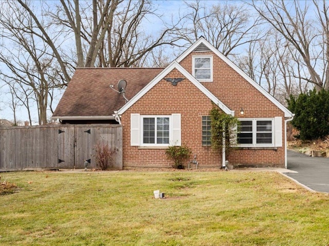 view of front facade with roof with shingles, a front lawn, and brick siding